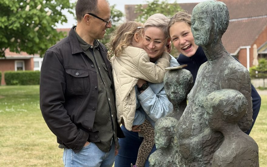 Familien Bøgeblad lytter og leger til Hanne Warmings skulptur Mor med Børn, der kan opleves på Halskov. 
